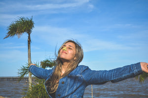 A woman stretching her arms out while wearing a green Nöz SPF sunscreen on her nose outside near a beach